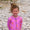 A smiling child in a UV Protective Long Sleeve Swimsuit Pink Starfish stands on a pebble beach, with curly hair in a bun.