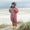 A child on a beach in an EcoSplash waterproof pink puddle suit with lightning bolts, wearing a hat and yellow wellies.