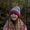 A smiling girl wearing a Striped Cable Bobble Hat in pink and blue, standing outside with railings in the foreground.