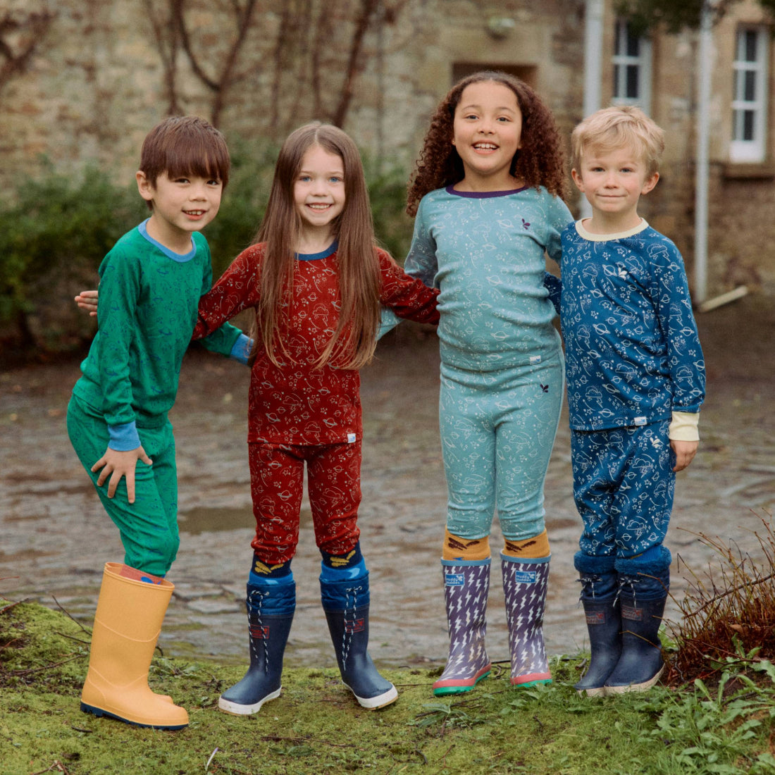 Four children in patterned thermal tops and wellies. One wears 'Kids Thermal Top Green' in a green outdoor setting.