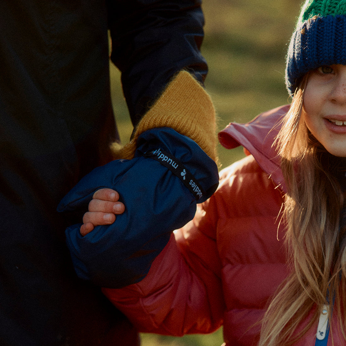 A child wearing a hat and pink coat holding hands with an adult wearing PU Mitts Navy Recycled Adult.