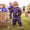 A young child wearing Muddy Puddles Children's Waterproofs plays outside in a garden with other kids, stirring mud in a bucket.