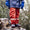 A child in Muddy Puddles waterproofs, wearing a blue coat, orange trousers, blue gloves and wellington boots, standing on a wet log in the rain.