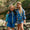 Two girls in Muddy Puddles Children's Waterproofs pose outdoors. One wears a blue jacket with yellow, paired with blue shorts.