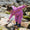 A child wearing Muddy Puddles Children's Waterproofs (a pink starfish patterned rain suit) bends to touch something on a rock on a rocky beach.