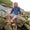 A boy wearing Muddy Puddles Children's Waterproofs is sitting on a rock, on a rocky beach with a grassy hill in the background.