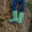Muddy Puddles waterproofs: A child in jeans and green lightning bolt wellies perched on a tree, roots visible.