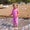 A young girl in Muddy Puddles Children's Waterproofs (purple with star design) stands on a beach as the tide comes in, smiling happily.