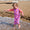 A young child, wearing a pink and orange Muddy Puddles swimsuit, paddles in the sea on a sandy beach, smiling joyfully.