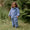 A child wears Muddy Puddles blue waterproofs with white lightning bolts in a grassy woodland setting. They're holding a stick.