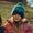 A child wearing a Muddy Puddles pink waterproof jacket and blue and green beanie smiles at the camera.