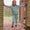 A smiling child stands in a doorway wearing Muddy Puddles Children's Waterproofs, a blue patterned pyjama set, with bare feet.