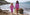 Two girls in UV safe swimwear, adorned with star patterns, stand on a beach rock, holding hands and smiling by the sea.
