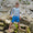 A boy wearing Muddy Puddlers! swimwear stands on rocks. He wears a colourful stripey top and star print blue shorts.
