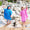 Two children on a beach in hooded Beach Towel Ponchos with star prints, waving to the camera.
