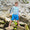 A boy smiling on rocks wearing UV Protective Swim Shorts Blue Starfish and a striped top, looking at the camera.