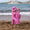 A child wearing a UV Protective Sun Hat Pink Starfish, stands on a sandy beach, back to camera, looking out at the waves of the sea.