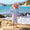 A child wearing a UV Protective Surf Suit Multi Stripe stands on rocks at the beach with the sea and cliffs in the background.