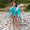 A girl on a pebble beach giving a thumbs up, wearing a UV Protective Long Sleeve Swimsuit Green Ice Cream and matching robe.