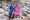 Waste reduction and circularity. Two children wearing hooded, star-patterned ponchos sit amongst rocks at the beach and smile at the camera.