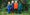 Muddy Puddles Originals: Four young children stand in a field, wearing waterproof overalls and jackets in blue, red, and green.