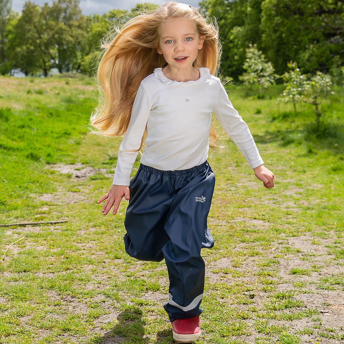 A young girl with long blonde hair runs across a grassy field wearing Puddleflex Waterproof Fleece Lined Trousers in navy.