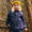 A little girl in a wood wearing a navy Rainy Day Waterproof Jacket and knitted hat, smiling at the camera.
