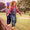 Two young girls balancing on a wall in a park. The girl in front wears green Originals Waterproof Dungarees and yellow boots.