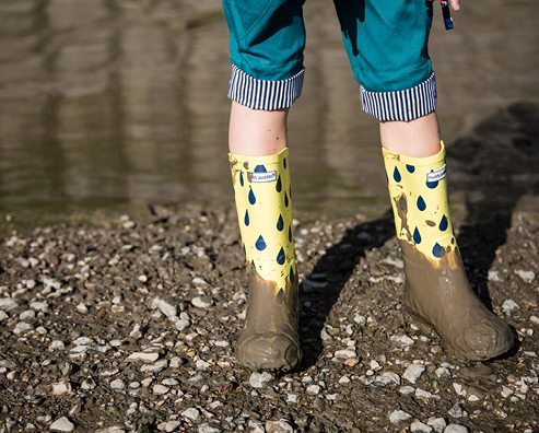 child stood on gravel wearing muddy wellies