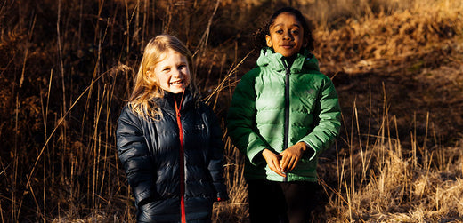 Two children in waterproof jackets outdoors in autumn grass, kids rainwear and outdoor clothing