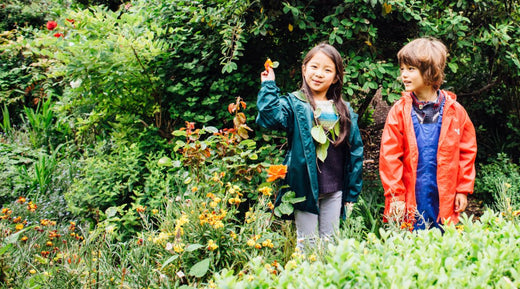 children stranding in garden, wearing vibrant muddy puddles green and red raincoats