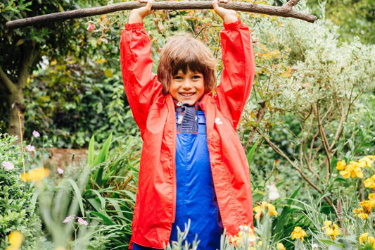boy holding long stick above his head, wearing vibrant muddy puddles waterproof jacket and dungarees