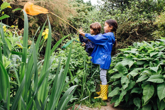 children fishing in a small pong using a long net, wearing muddy puddles waterproofs