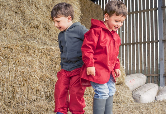 boys standing on hay bale in barn, wearing red muddy puddles waterproof jacket and trousers