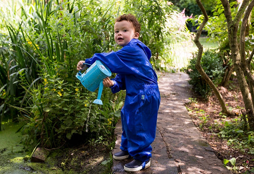 boy stood by a pond holding a blue watering can, wearing a vibrant blue puddlesuit