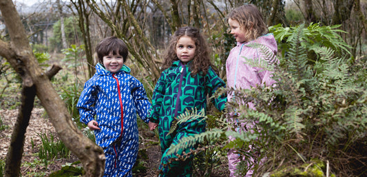 Children wearing colorful waterproof rain suits playing outdoors in a forest setting