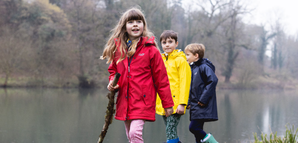 Children wearing waterproof jackets exploring outdoors by a lake in autumn