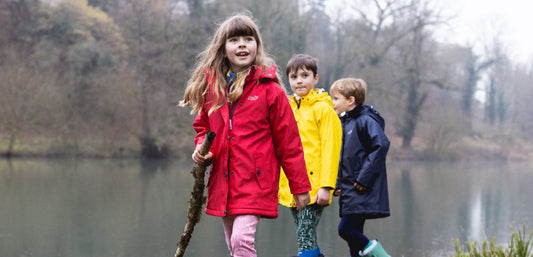 Children wearing waterproof jackets exploring outdoors by a lake in autumn