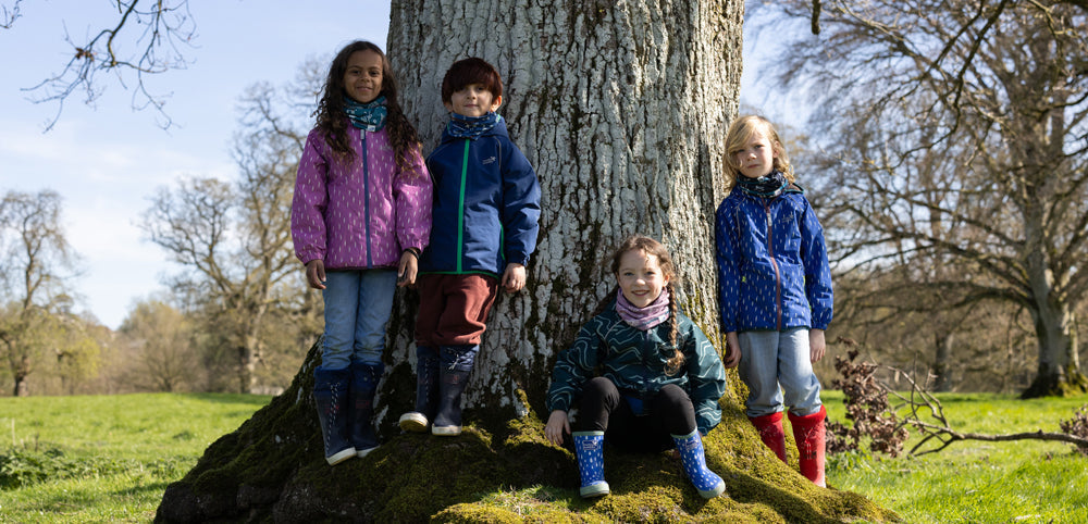 group of children standing in front of tree wearing muddy puddles ecosplash waterproof jackets