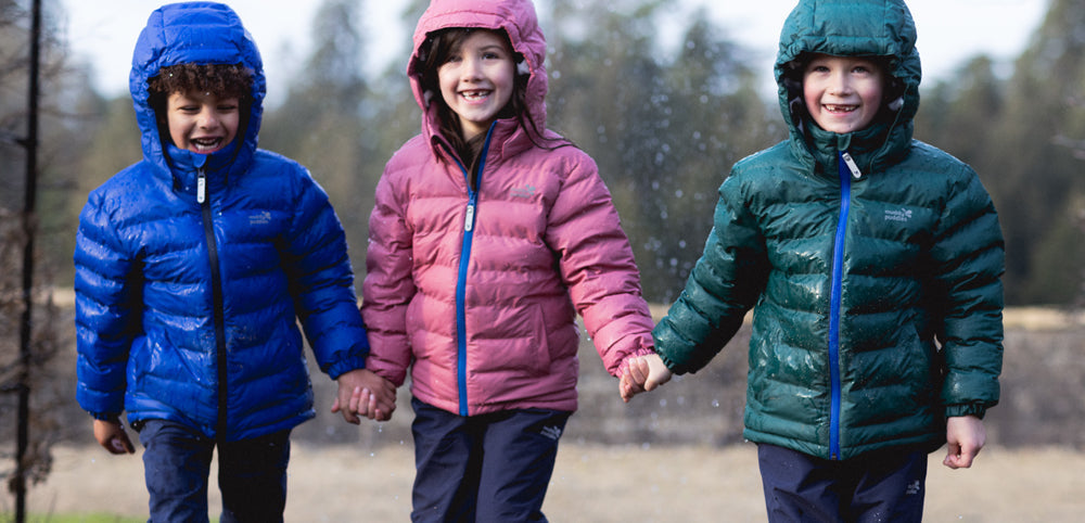 Three kids in colorful waterproof jackets and trousers playing outdoors in autumn