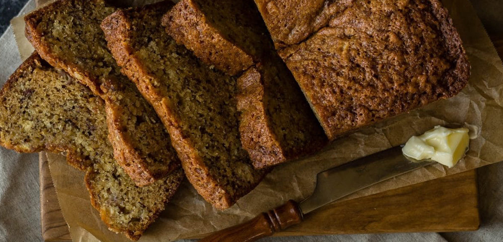 banana bread on a wooden chopping board with a knife and butter
