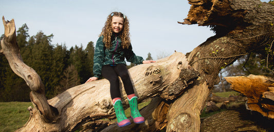 girl sitting on fallen tree, wearing muddy puddles waterproof jacket and boots