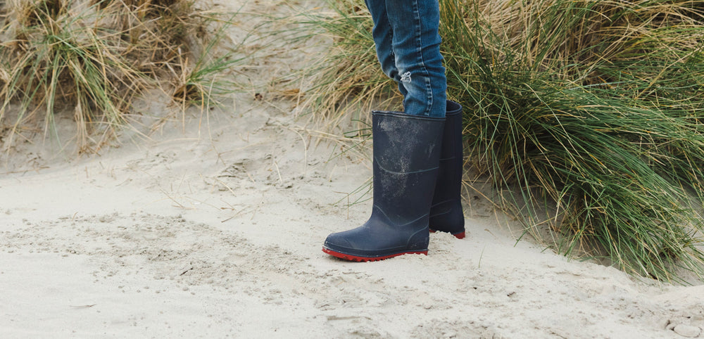 boy wearing navy wellies standing on grassy sand dunes