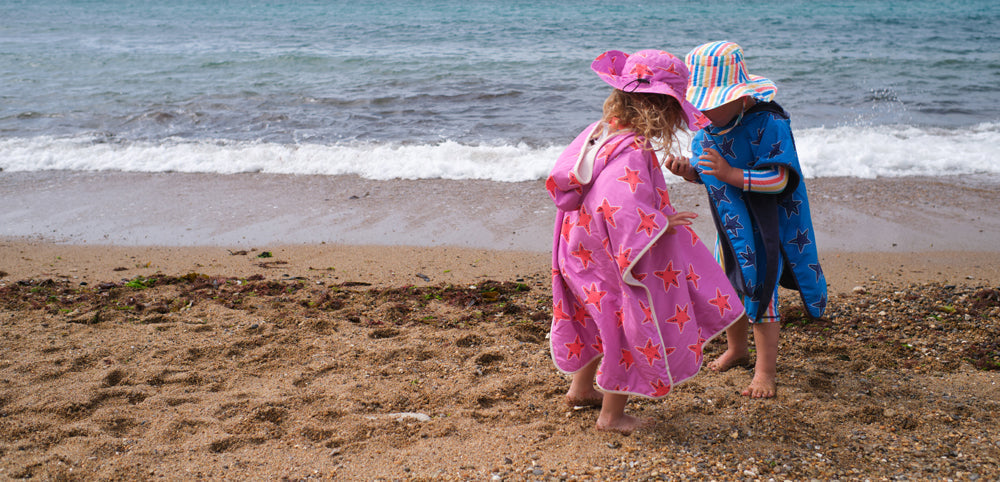 boy and girl on sandy beach wearing vibrant muddy puddles towel ponchos and sun hats