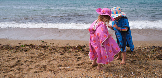 boy and girl on sandy beach wearing vibrant muddy puddles towel ponchos and sun hats