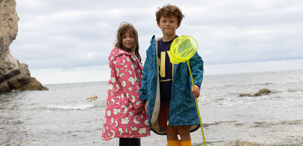 Children wearing colorful waterproof jackets by the seaside, boy holding a yellow net