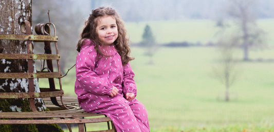 girl sat underneath tree in country park wearing muddy puddles pink raindrop print puddle suit
