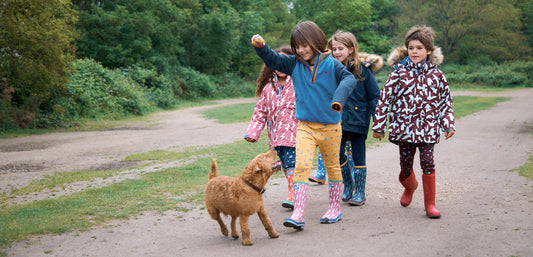 Children wearing colorful waterproof jackets and wellies walking outdoors with a dog
