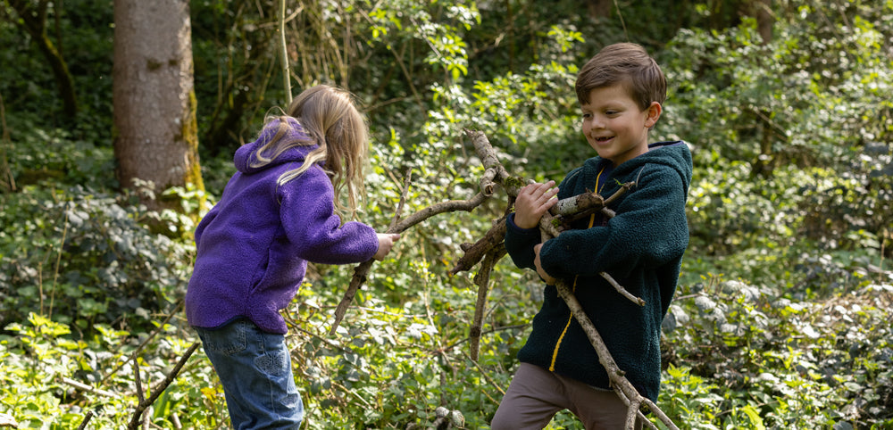 boy and girl collecting sticks, wearing green and purple muddy puddles borg fleeces
