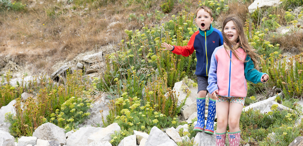 boy and girl stood by hillside wearing colourful fleece jackets and wellies by muddy puddles